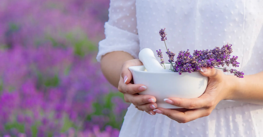 Frau in weißem Kleid hält einen Mörser mit frischen Lavendelblüten im Lavendelfeld – natürliche Aromatherapie und Entspannung