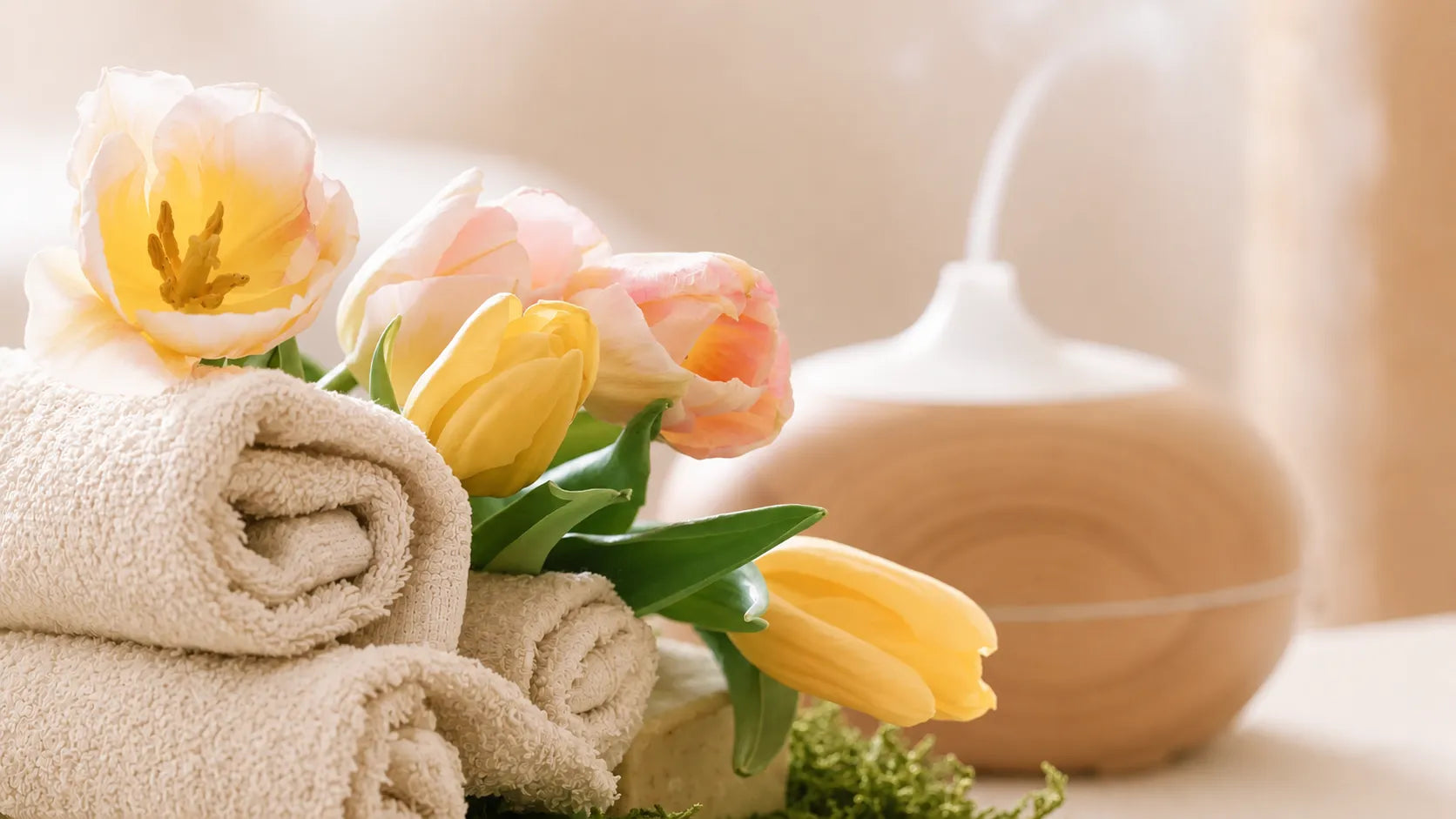 Entspannende Aromatherapie-Szene mit Handtüchern, Blüten und Diffuser in warmen Naturtönen.