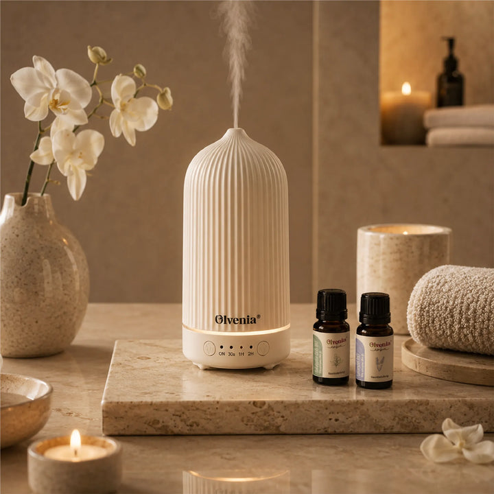 Olvenia Keramik-Diffuser mit Duftnebel neben ätherischen Ölen, Orchideen, Kerzen und Handtüchern im Spa-Ambiente