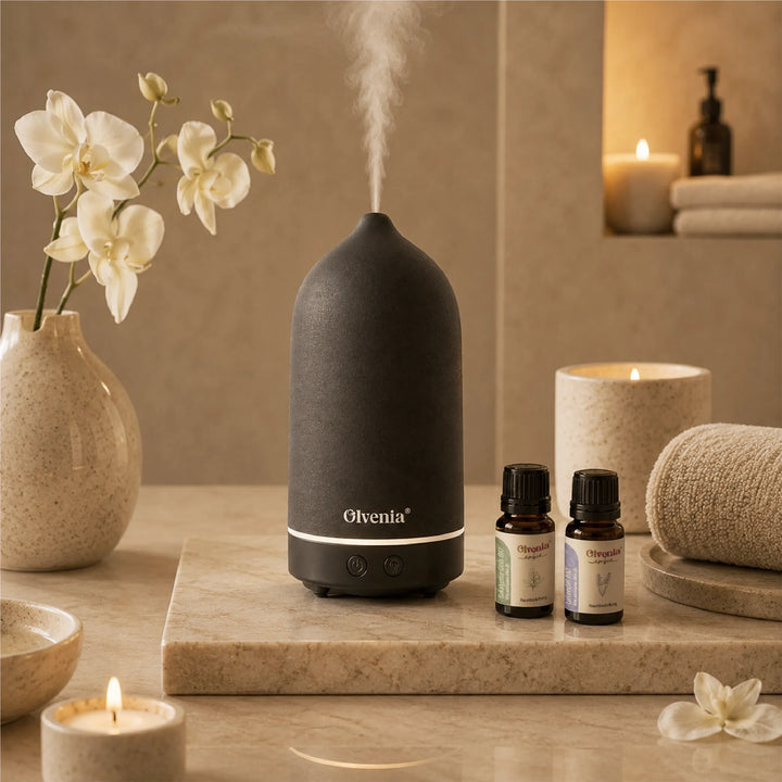 Schwarzer Olvenia Keramik-Diffuser mit Duftnebel neben ätherischen Ölen, Orchideen, Kerze und Handtüchern im Spa-Ambiente